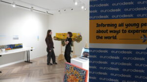 Íslenska: Tvær ungar konur ræða saman við listaverk á sýningu í Hinu Húsinu með Eurodesk veggspjaldi í forgrunni. English: Two young women talk in front of an artwork at an exhibition in Hitt Húsið, with a Eurodesk banner in the foreground.