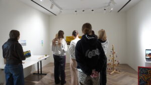 Íslenska: Hópur ungmenna skoðar sýningu á listaverkum og skapandi verkefnum ungs fólks. English: A group of youth observe an exhibition of creative works and youth-made art projects.
